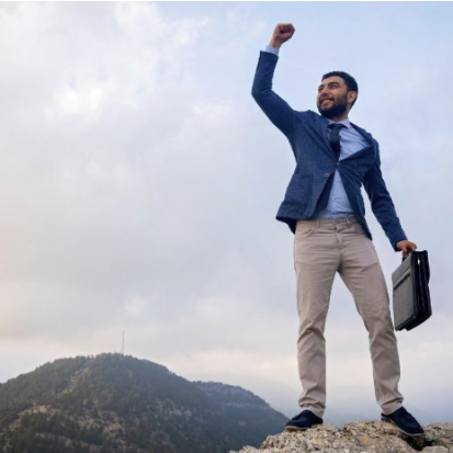 A person in business A person in business attire standing confidently on a rocky peak, holding a briefcase and raising a fist triumphantly. The scene conveys themes of overcoming challenges and transforming insecurity into an advantage.